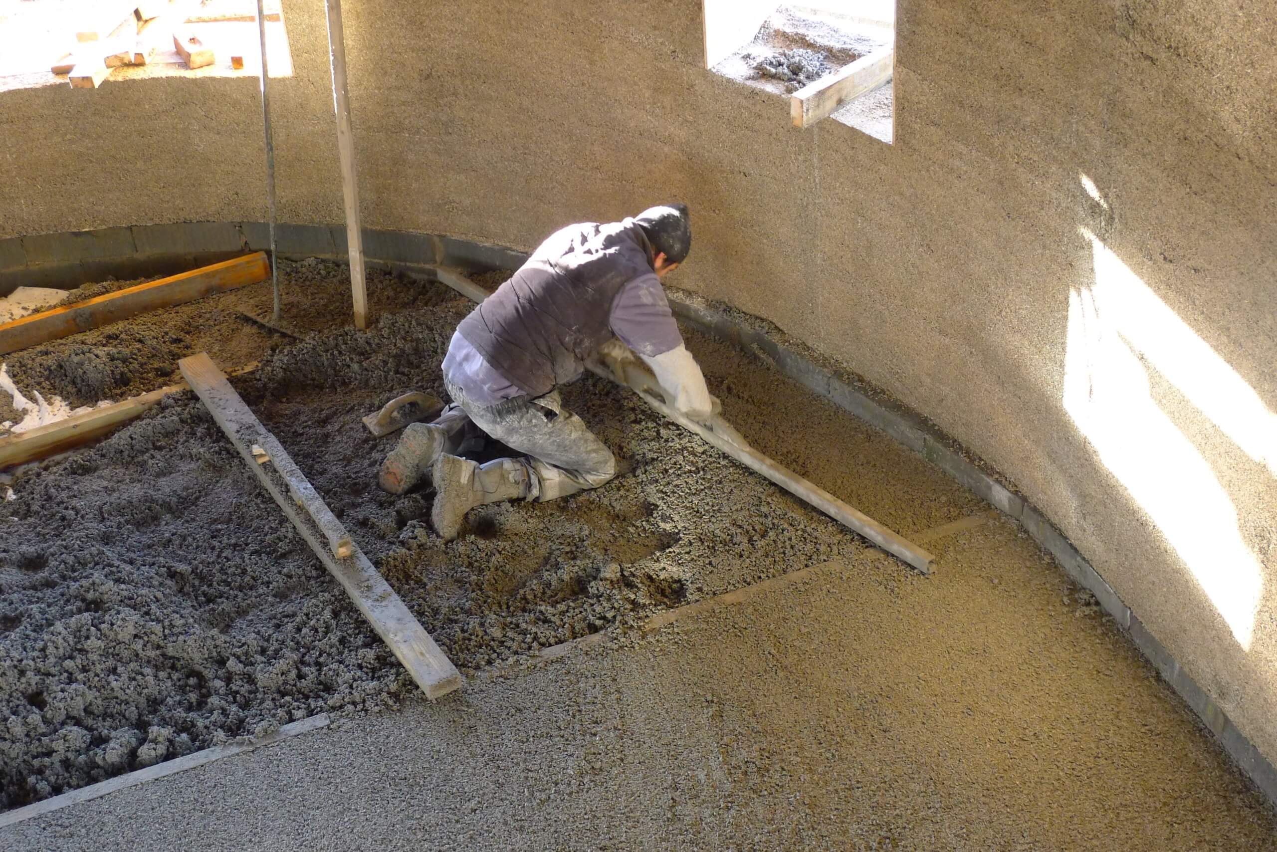 labourer levelling a lime-sand screed floor above hempcrete floor and surrounded by hempcrete walls